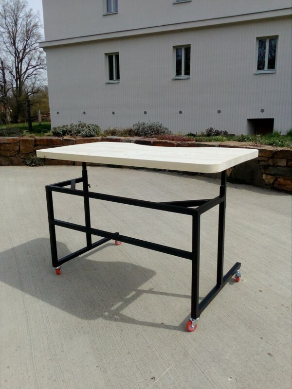 Tříčtvrtinový pohled na mobilní stolek pro vozíčkáře postavený na betonové venkovní ploše před budovou